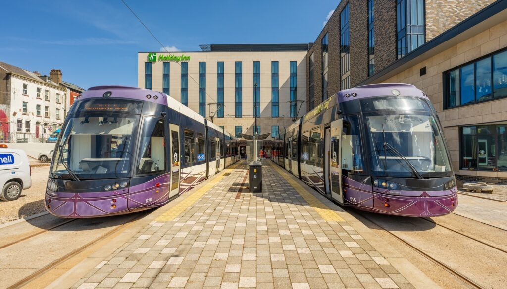 A photo showing two purple trams at a station surrounded by a Holiday Inn hotel