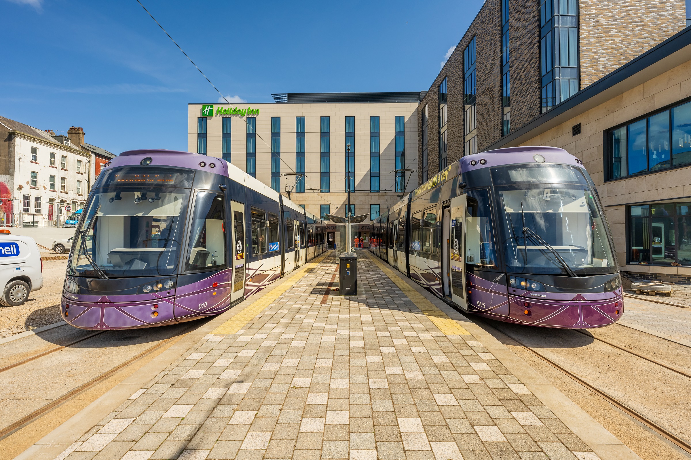 A photo showing two purple trams at a station surrounded by a Holiday Inn hotel
